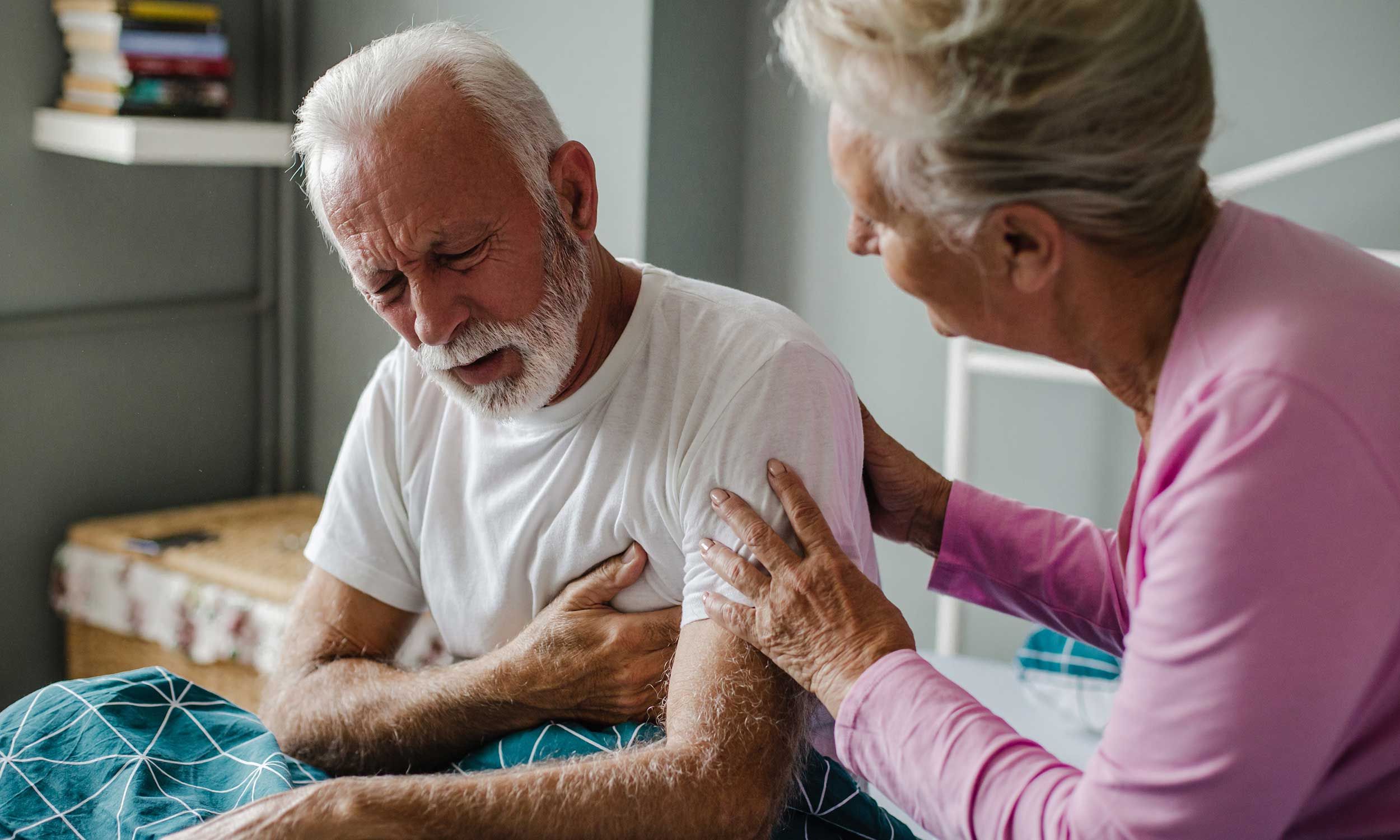 A man with heart disease, clutching his chest with wife next to him